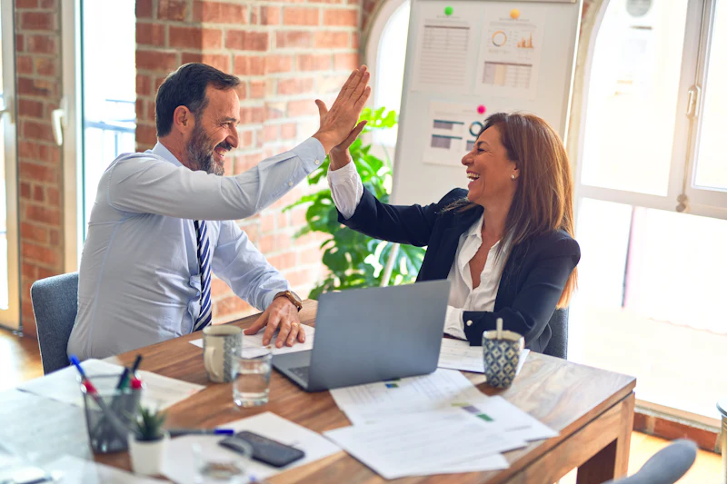 Two colleagues high-fiving across a desk after a successful meeting