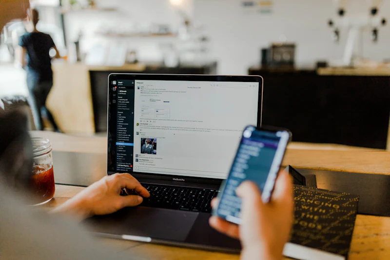 Hands holding a smartphone in front of a laptop